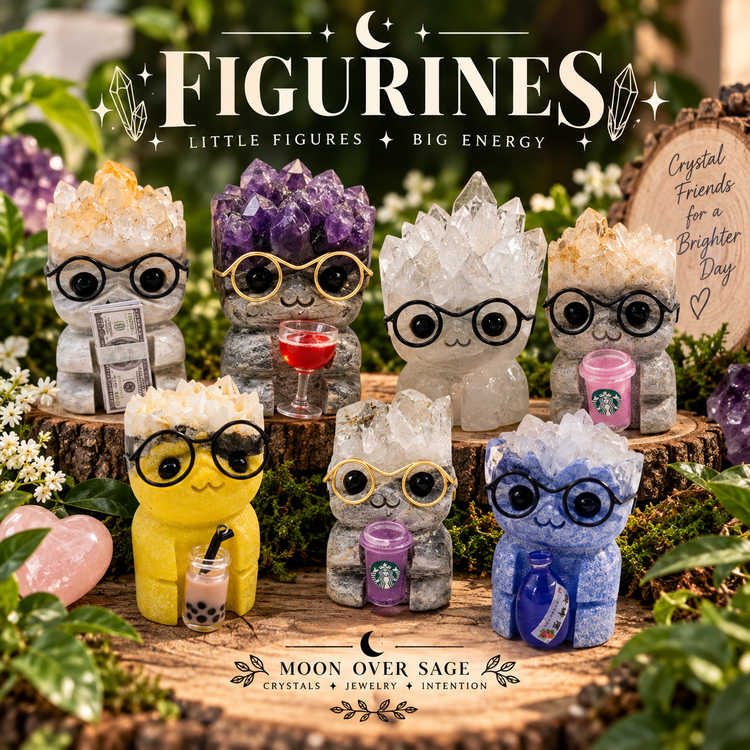Crystal figurines with gemstone clusters, glasses and playful accessories displayed in a woodland setting for the Moon Over Sage Figurines collection