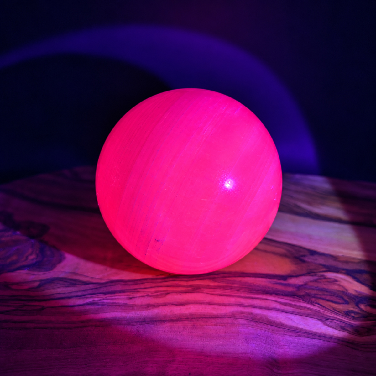 Pink Calcite crystal sphere glowing bright pink under UV light showing strong fluorescence